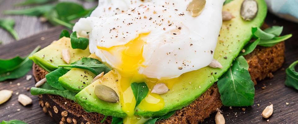 Avocado sandwich topped with egg on rustic table setting