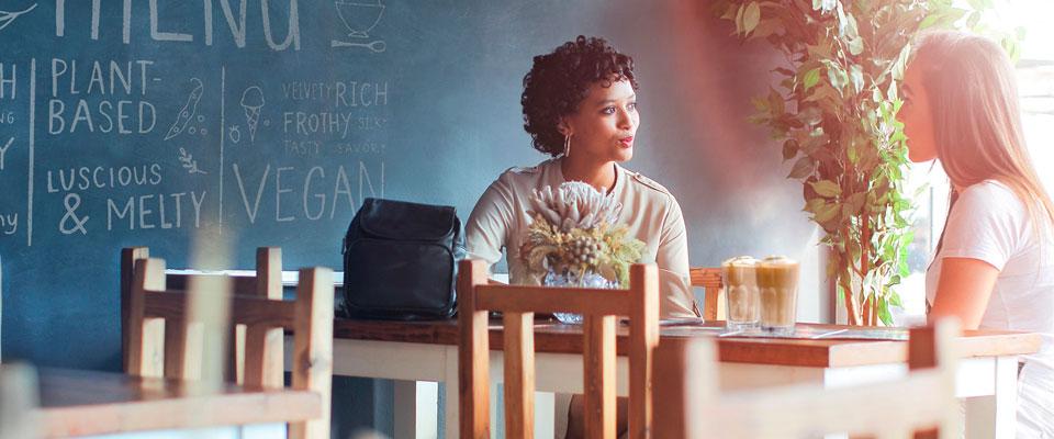 Two women sitting at a table chatting over tall lattes