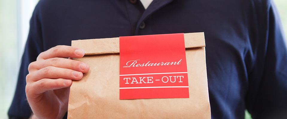 Person holding brown bag of take-out food
