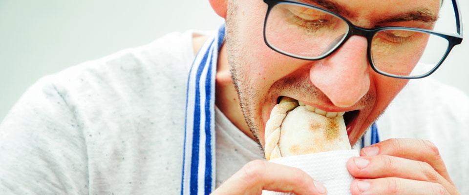 Close up of a man eating an empanada with his hands