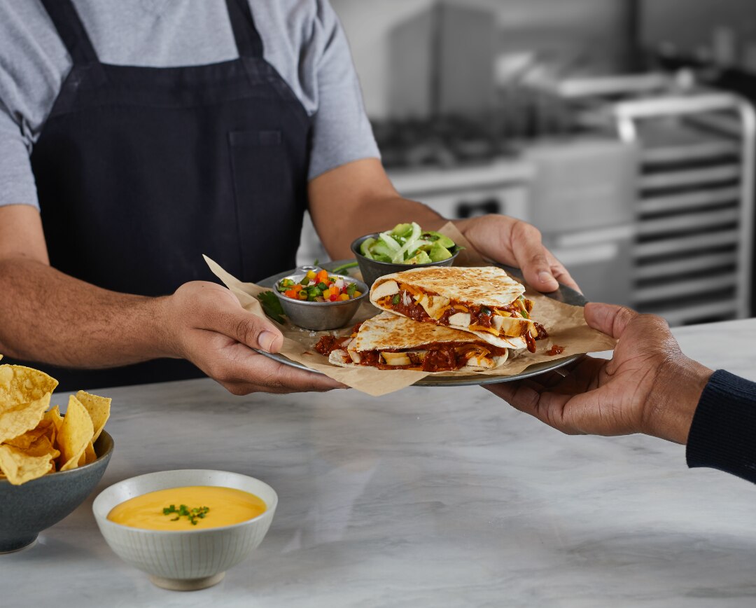 CM_BrandCorner_HeaderImage@2x.png Chef handing sandwich with soup over counter