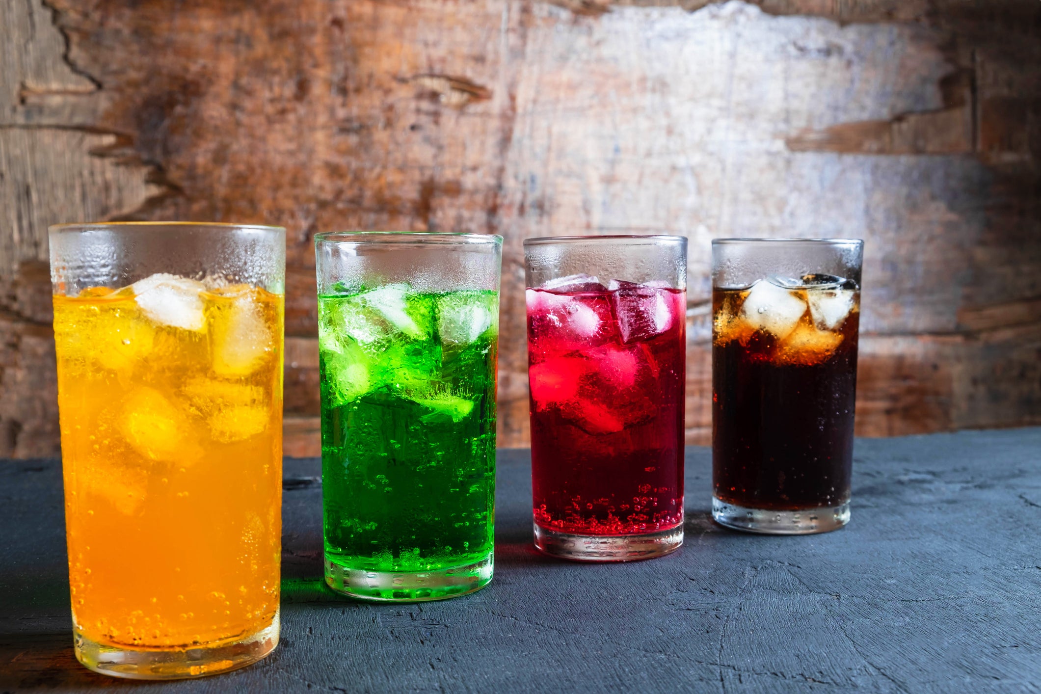 4 beverages shown at a diagonal - one yellow, one green, one red and one that looks like black cola