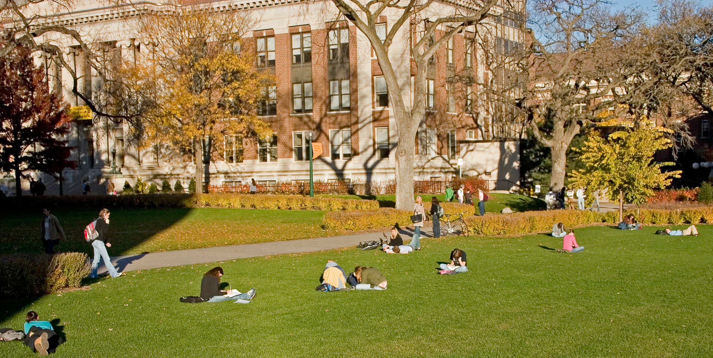 University campus with an old building in the background and college students reading books on the lawn