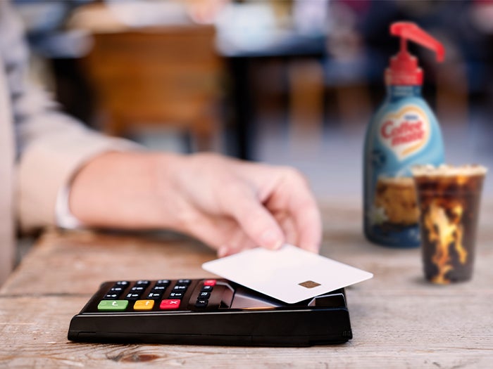 hand holding a credit card, paying for iced coffee with Coffee mate French Vanilla bulk creamer