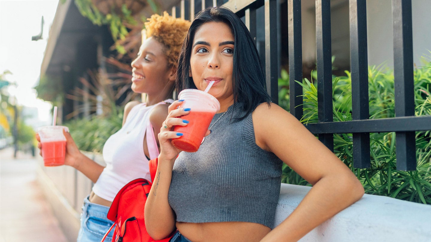 two women standing outside with a fruit beverage in their hands