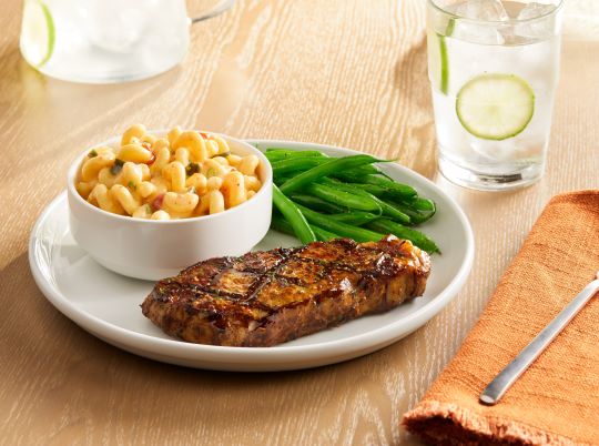 southwest style macaroni and cheese on a white plate with steak and green beans