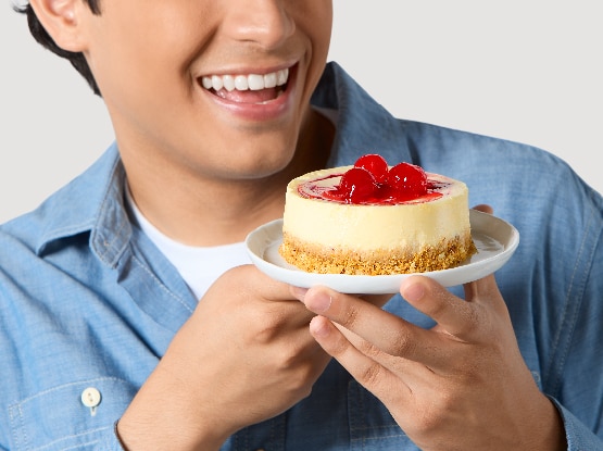 man smiling while holding a plate with a strawberry topped cheesecake