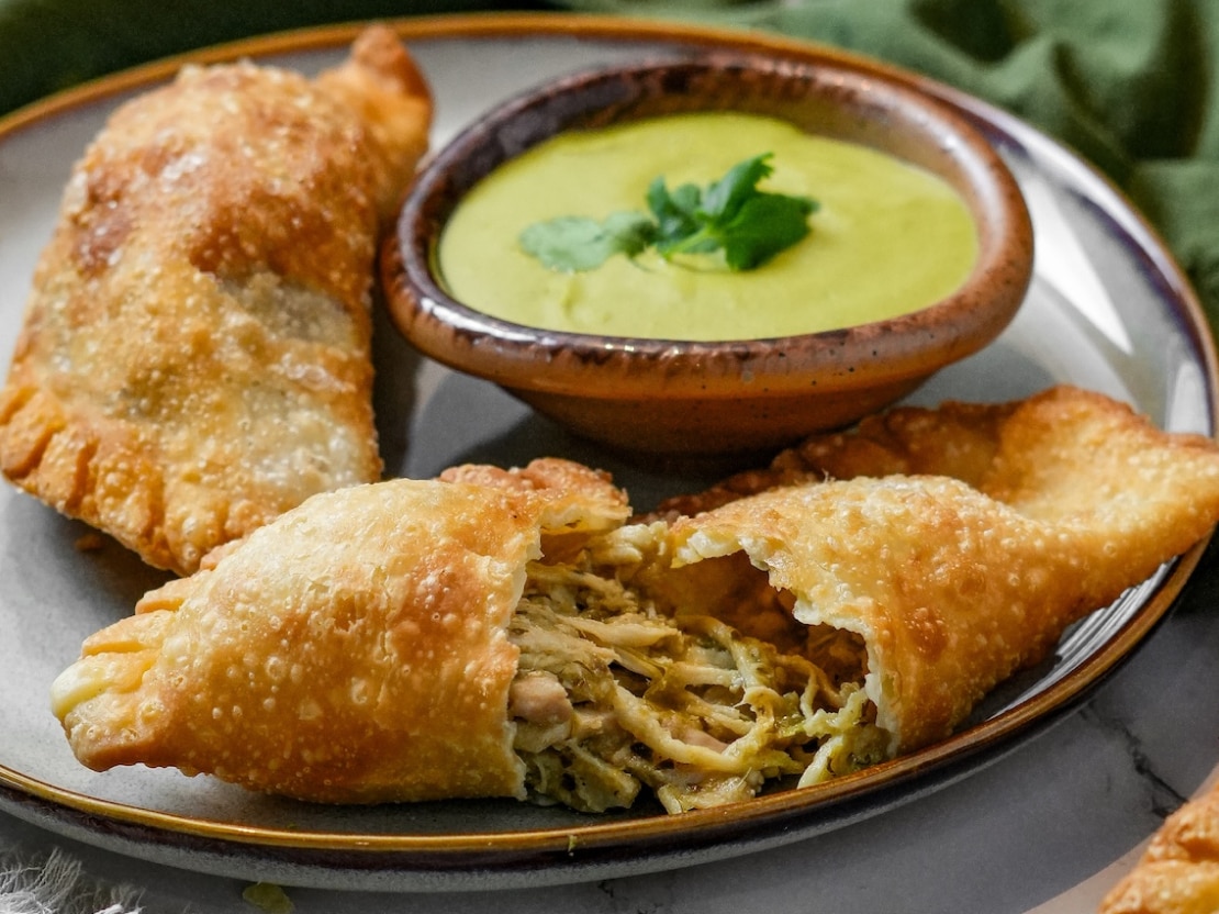 two empanadas on dish with bowl of dipping sauce