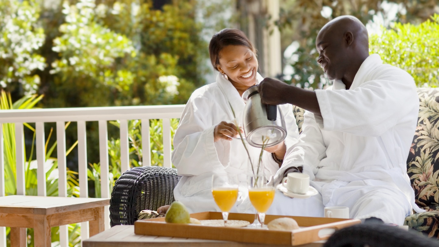 Two hotel guests in robes enjoying coffee and fresh juice on an outdoor patio as part of a hotel beverage program.