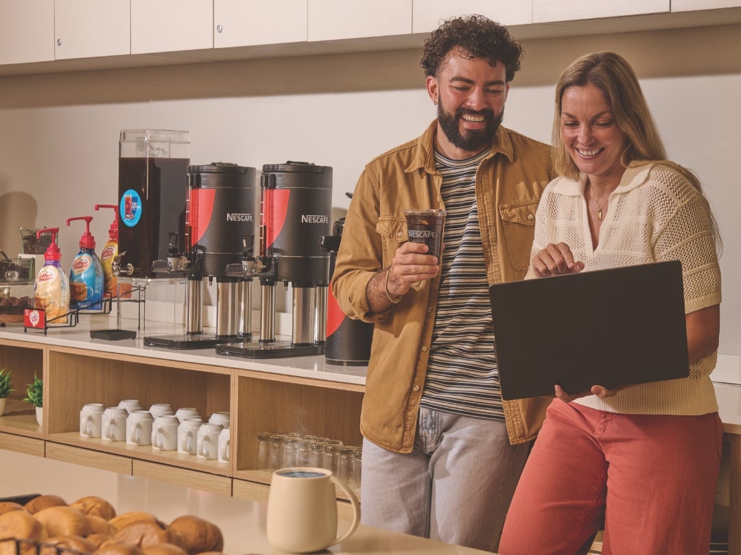 woman with laptop and man next to coffee machines