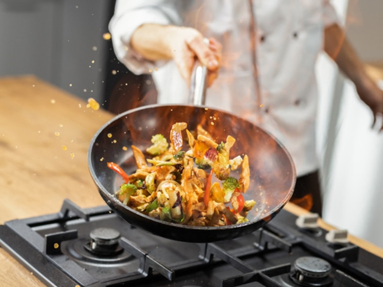 chef tossing vegetables in frying pan