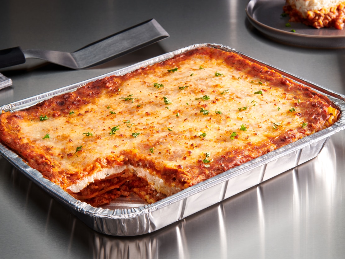 A large tray of lasagna with a single corner cut out
