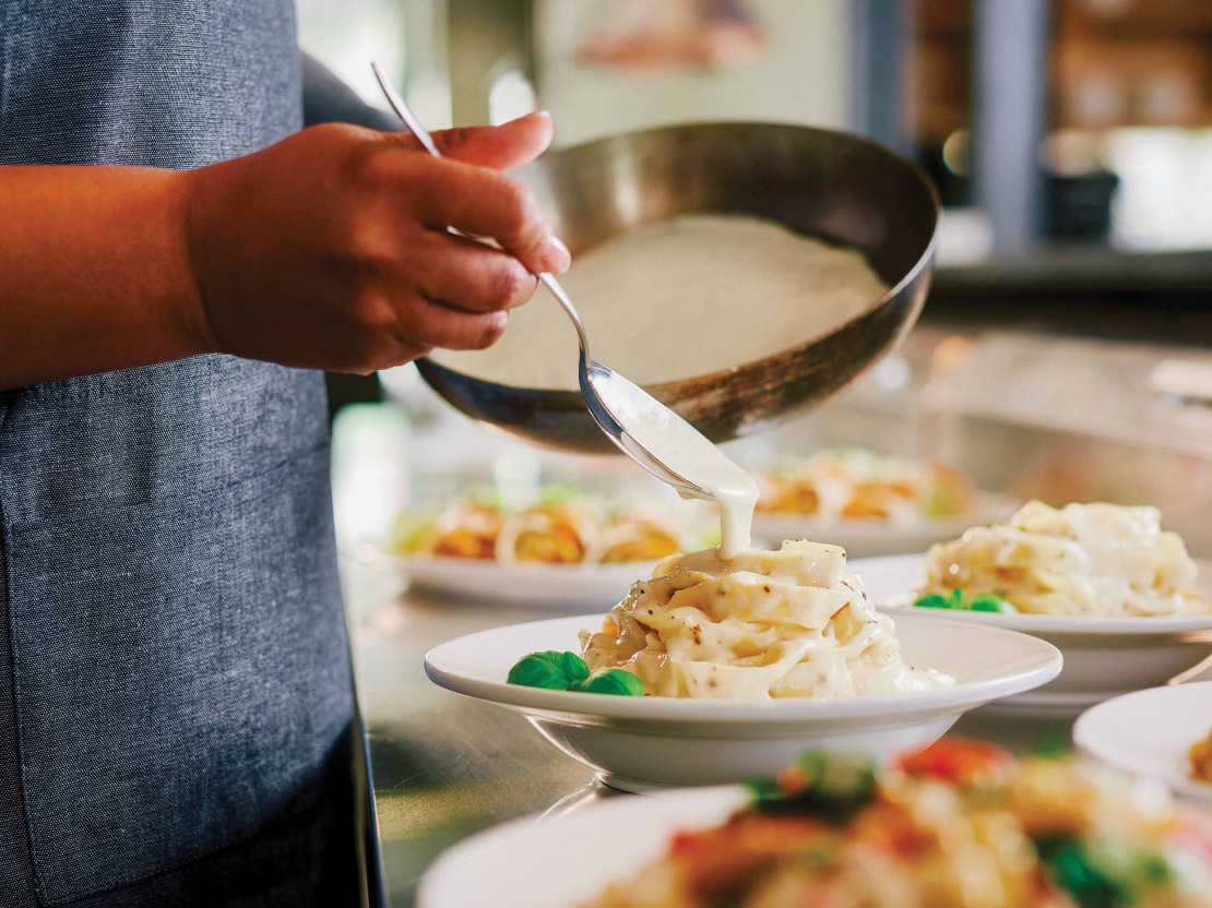 A chef adding sauce to a dish directly from a pan