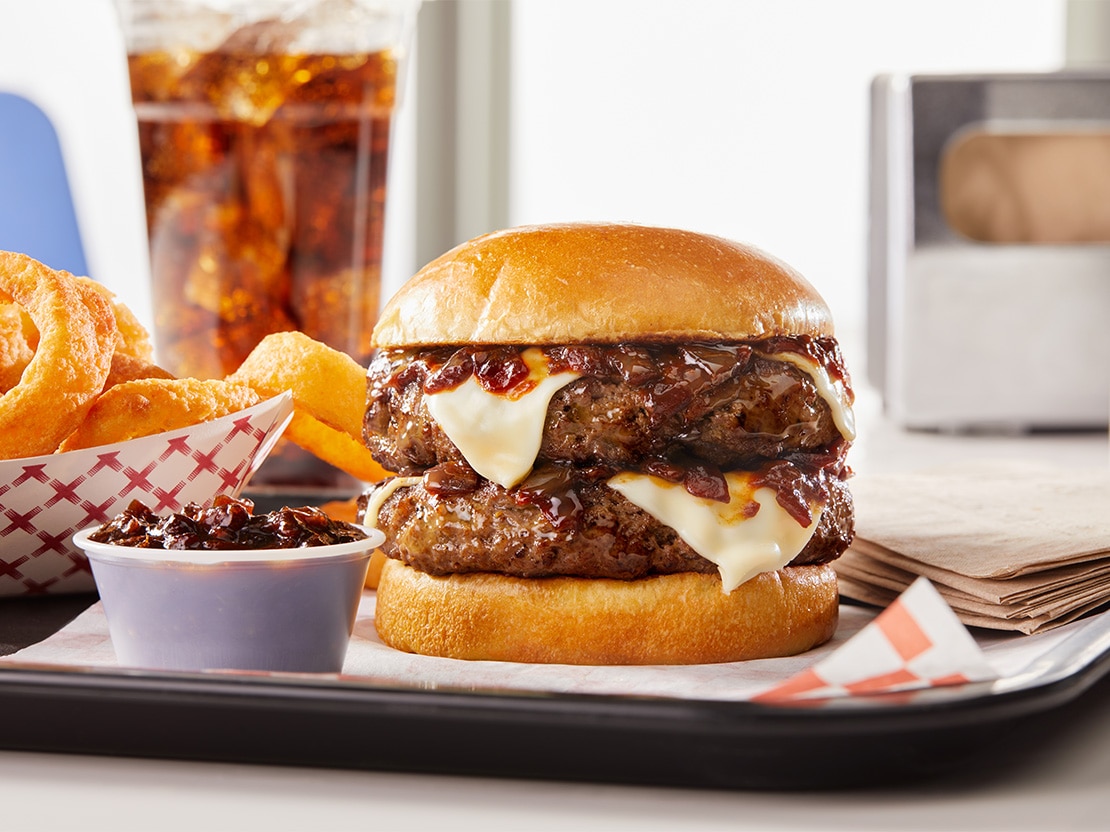 A large pub-style burger with two patties on a tray with onion rings