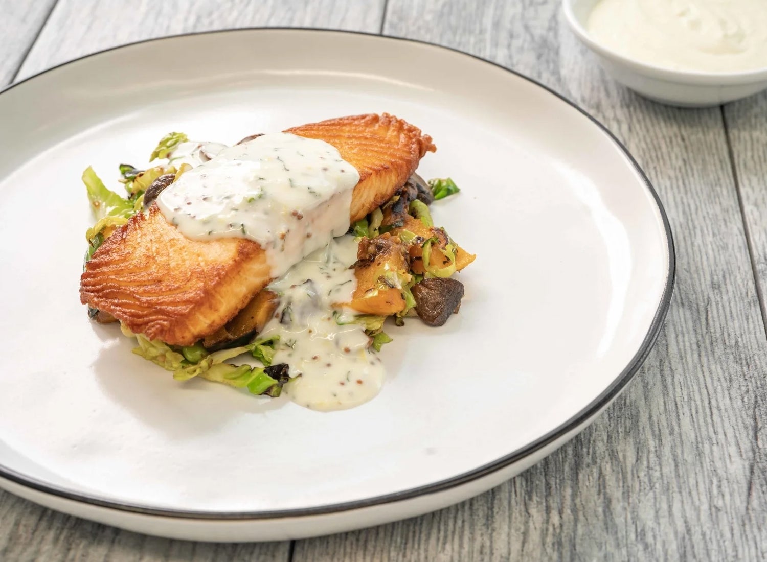 Salmon on a salad with white sauce on a plate.