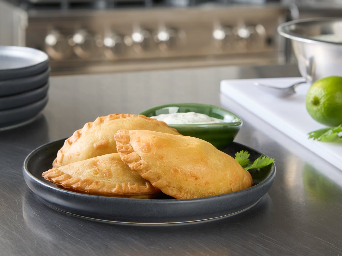 Three empanadas on a plate with a bowl of sauce