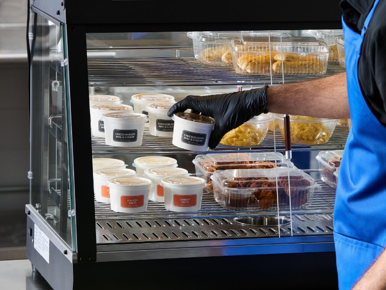Employee stocks packaged prepared foods in a refrigerated display case.​