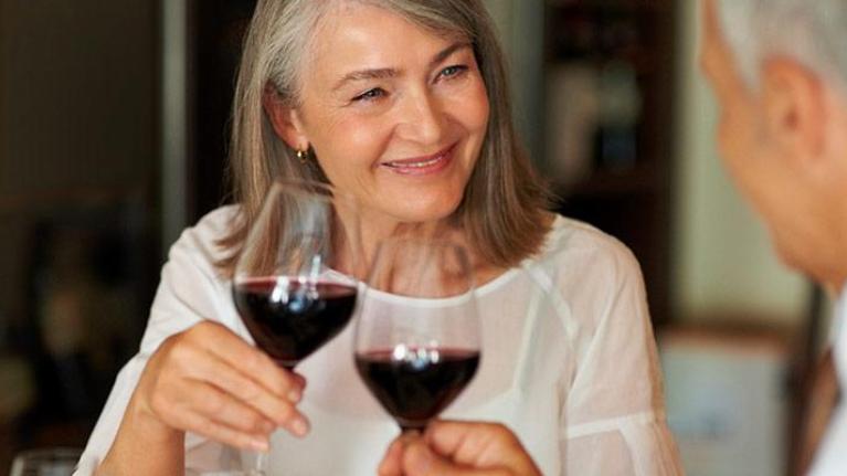 Two baby boomers at a restaurant drinking a glass of red wine