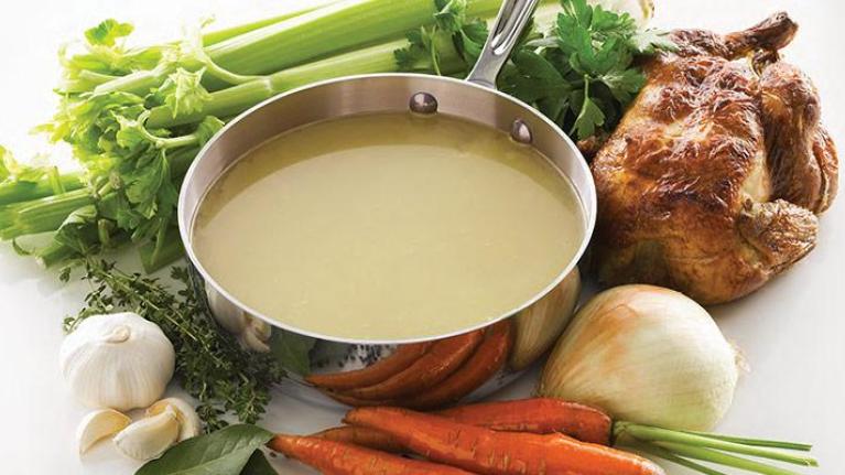 Pot of chicken stock with roasted chicken and assorted produce
