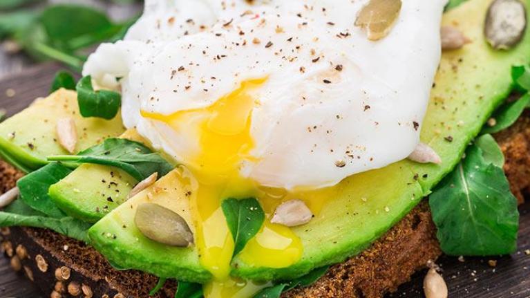 Avocado sandwich topped with egg on rustic table setting