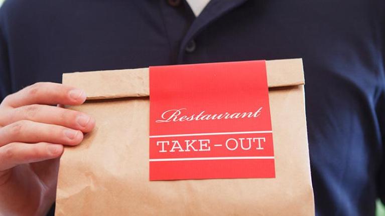 Person holding brown bag of take-out food