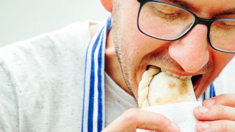 Close up of a man eating an empanada with his hands