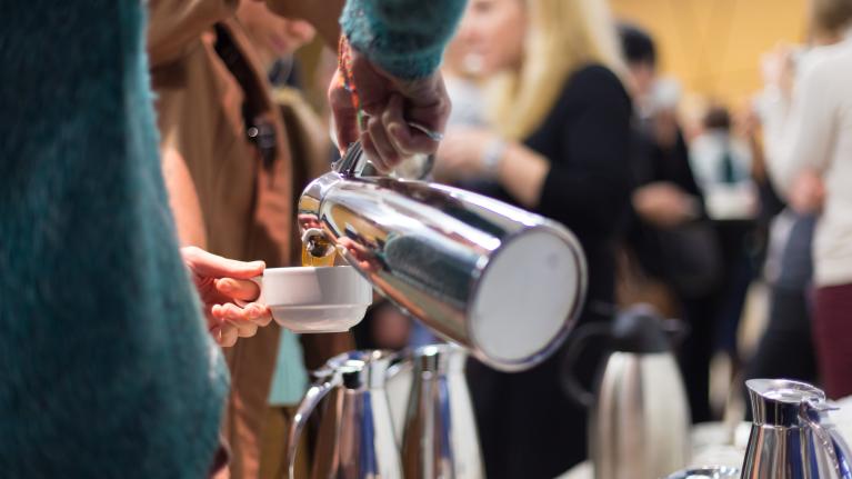 Person pouring from a carafe in a crowded dining hall