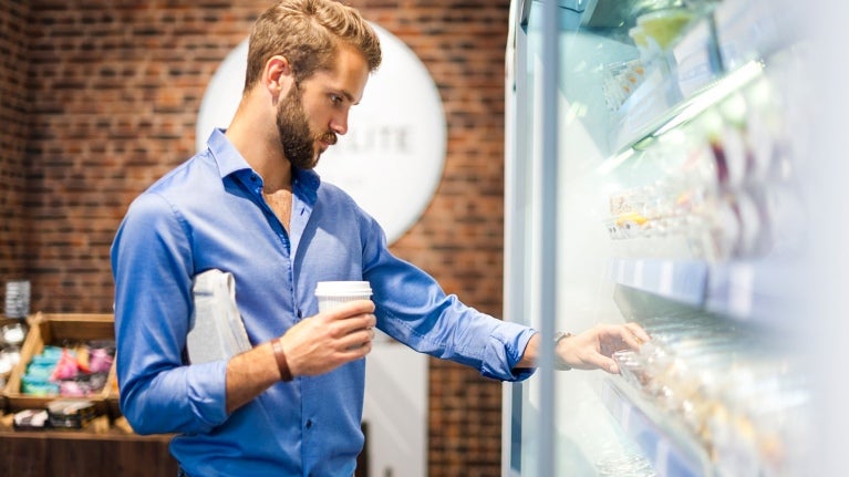 Man with coffee in hand selection something from refrigerated case