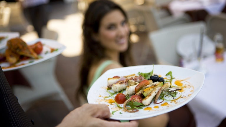 Close-up of 2 appetizers on white plates with a blurred woman in the background