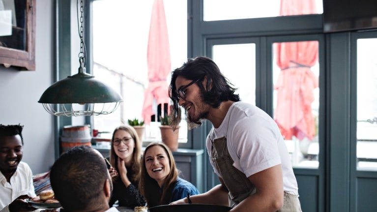 4 people sitting down at a restaurant with a waiter talking to them