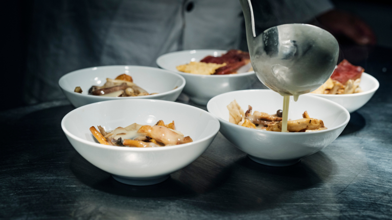 Five small bowls of food in white dishes with sauce poured over