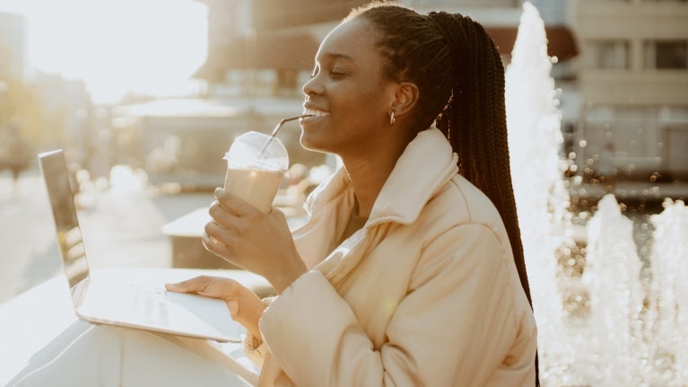 woman drinking iced coffee in front of open laptop