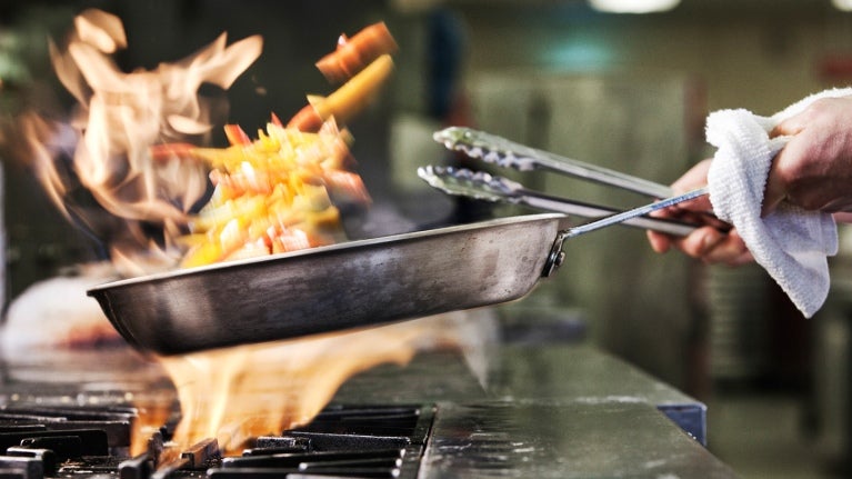 chef holding pan over open flame