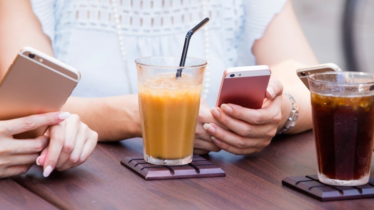 women sitting at table with juice in glass holding cell phones 