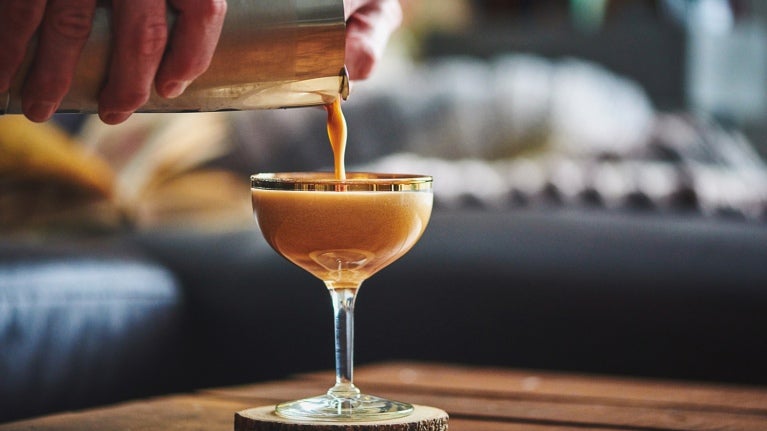 man pouring a drink from a shaker into a long-stemmed glass