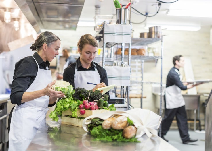 Two female chefs in a professional kitchen with fresh food on the table
