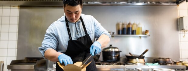 chef in kitchen adding food to a take out container