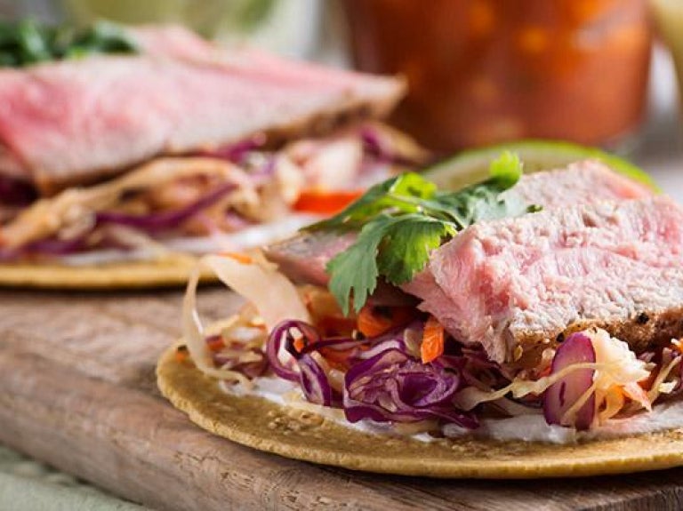 Wooden platter of fish tacos with sides of salsas