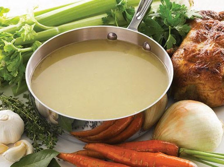 Pot of chicken stock with roasted chicken and assorted produce