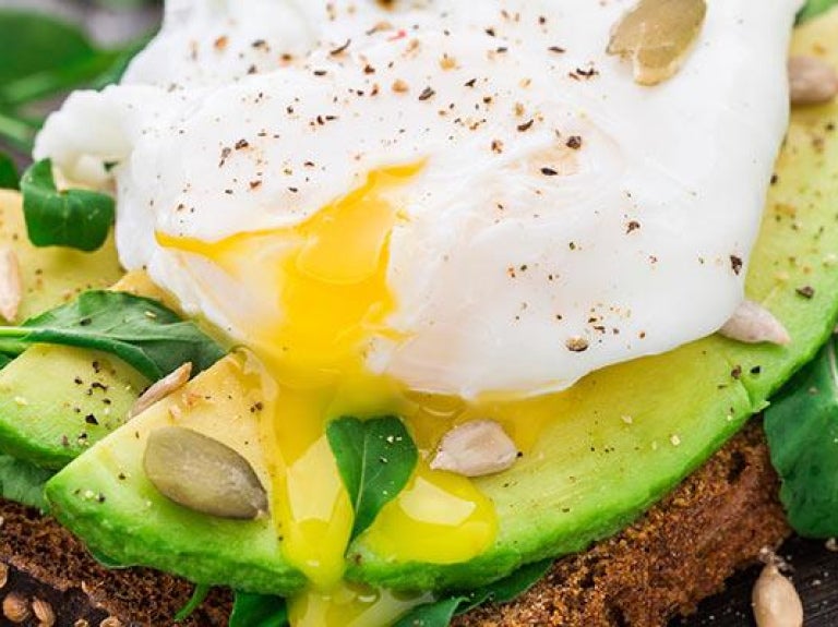 Avocado sandwich topped with egg on rustic table setting