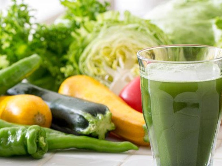 Two glasses of green vegetable juices in front of a display of vegetables
