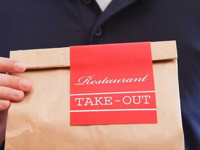 Person holding brown bag of take-out food