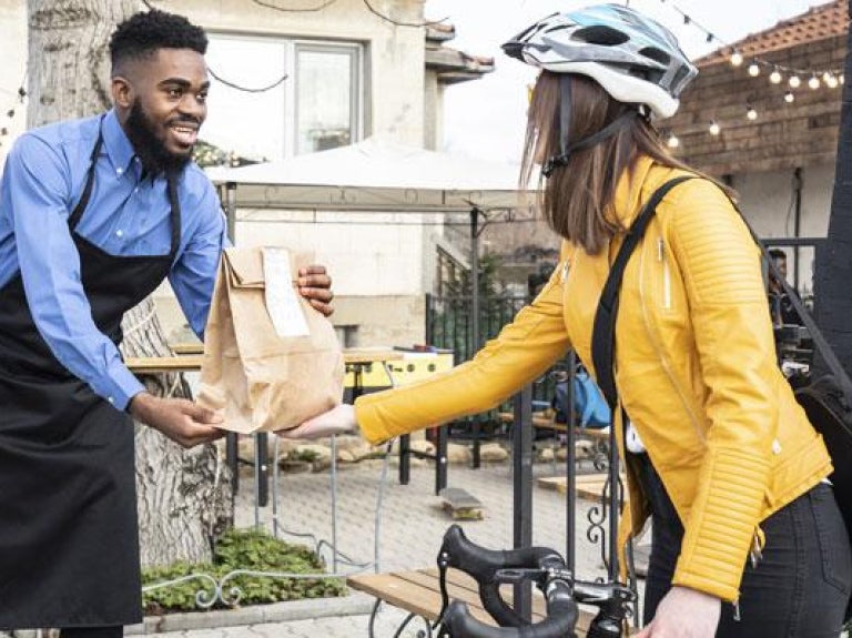 Man wearing apron handing BBQ takeout to a woman on a bicycle