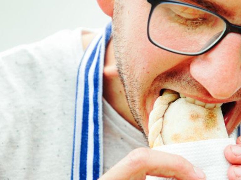 Close up of a man eating an empanada with his hands