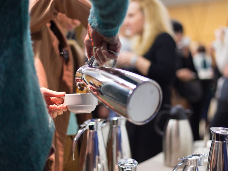 Person pouring from a carafe in a crowded dining hall