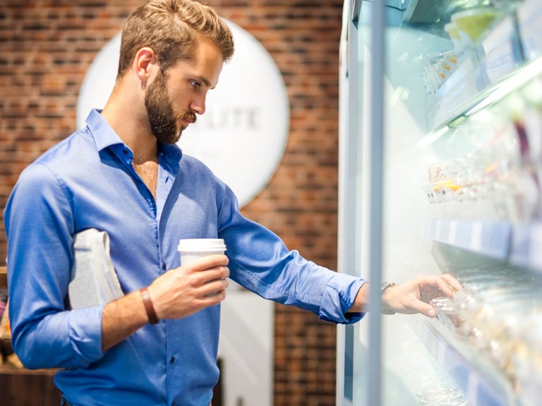 Man with coffee in hand selection something from refrigerated case