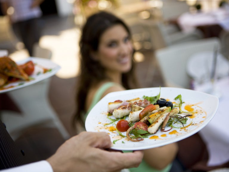 Close-up of 2 appetizers on white plates with a blurred woman in the background