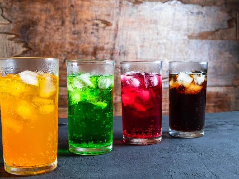 4 beverages shown at a diagonal - one yellow, one green, one red and one that looks like black cola