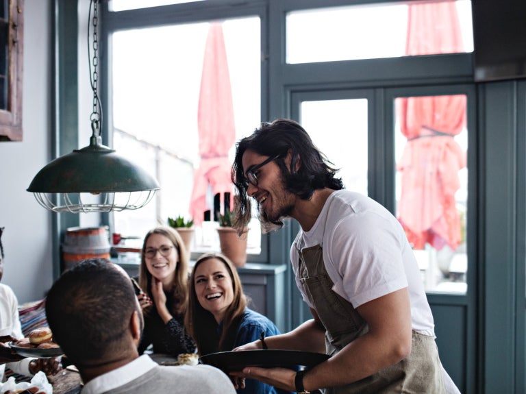 4 people sitting down at a restaurant with a waiter talking to them