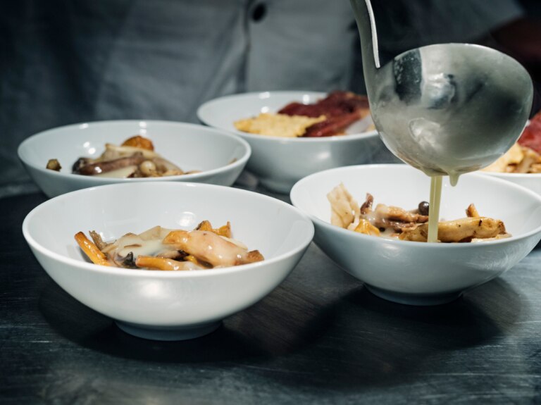 Five small bowls of food in white dishes with sauce poured over